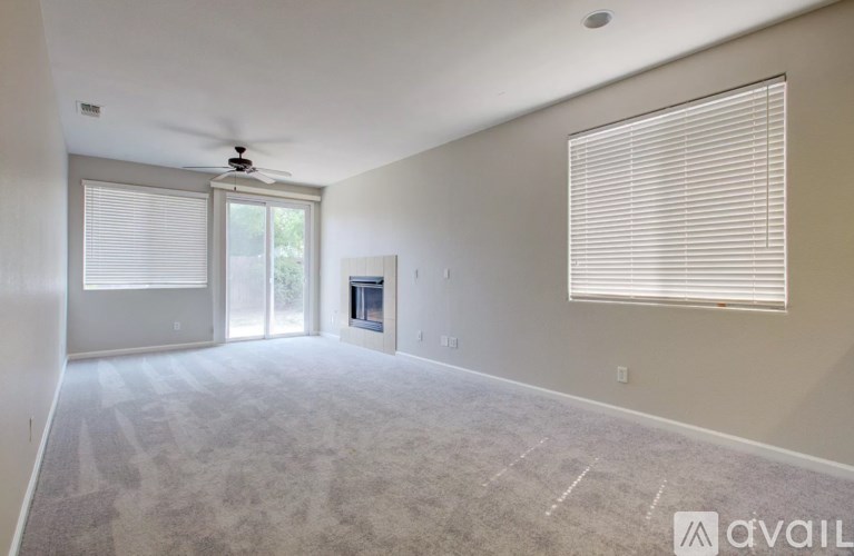 A spacious room with a carpeted floor, a ceiling fan, and a window with blinds.