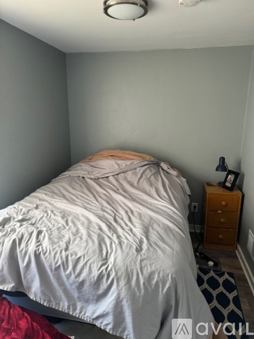 A bed with white sheets and a white pillow is in a room with a wooden nightstand.