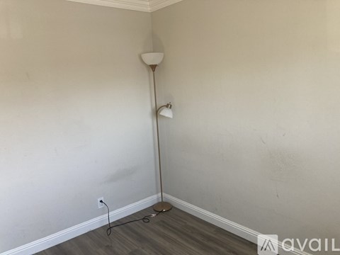 A lamp stands in a corner of a room with a white wall and wooden floor.