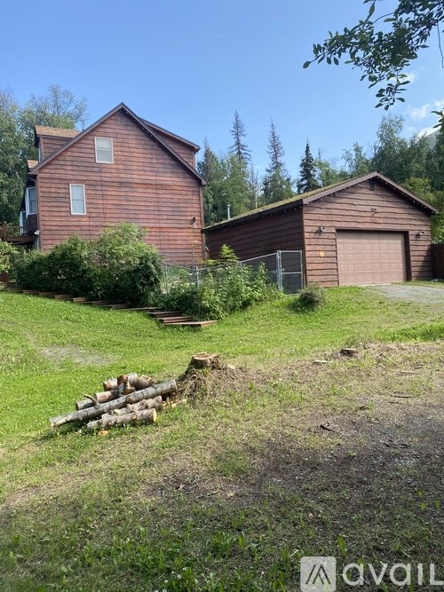 A wooden house with a garage and a fence is surrounded by greenery.