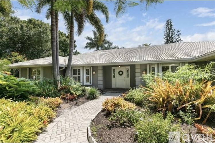 A house with a grey roof and a white door surrounded by green plants.