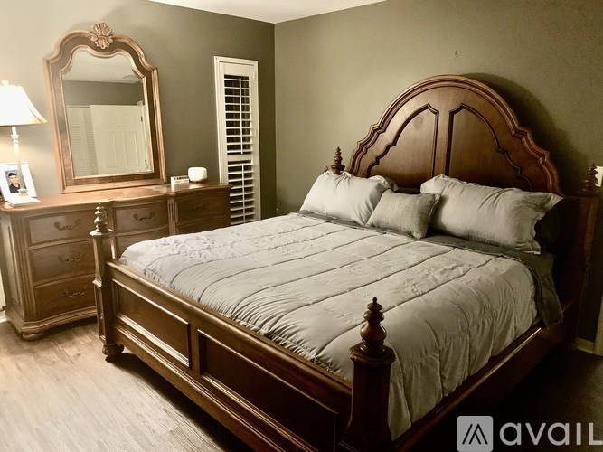 A bedroom with a large bed, a wooden dresser, and a mirror.