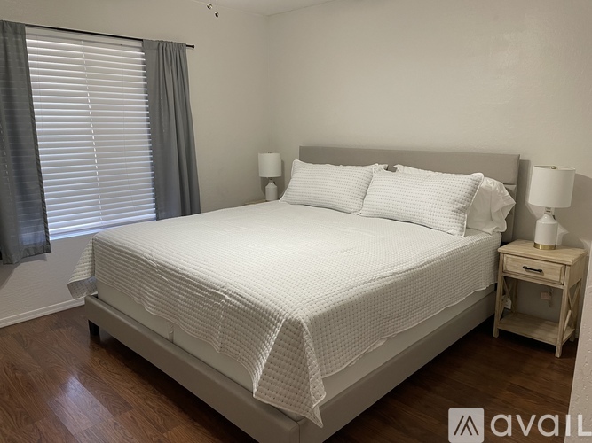 A white bed with a white bedspread and pillows in a room with wooden floors.
