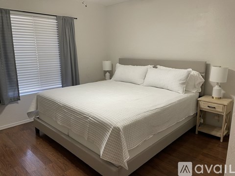 A white bed with a white bedspread and pillows in a room with wooden floors.