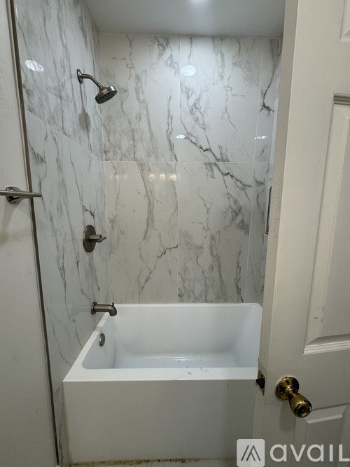 A white bathtub with a shower head and a door with a gold handle.
