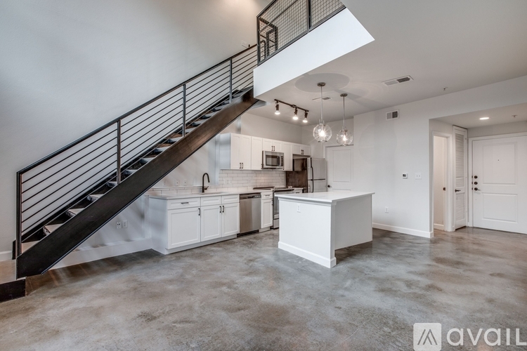 A spacious, empty room with a staircase and a kitchen area.