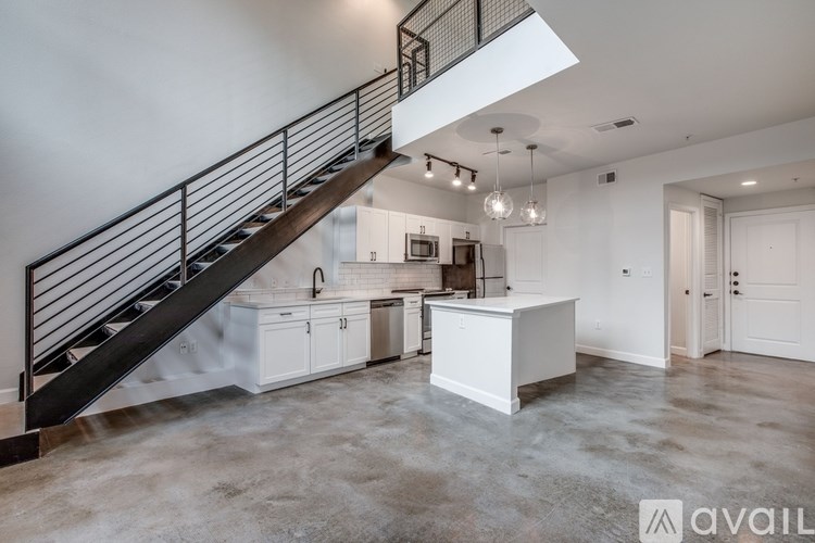 A spacious, empty room with a staircase and a kitchen area.