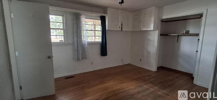 A room with wooden floors and white walls, with a window covered by a white curtain.