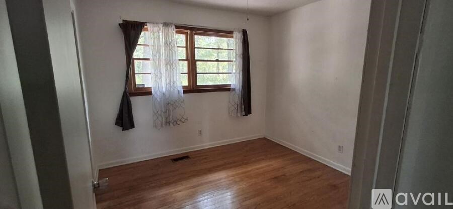 A room with wooden floors and a window with curtains.