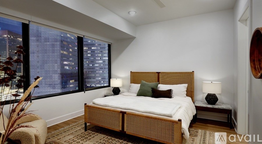 A bedroom with a large bed and a city view through the window.