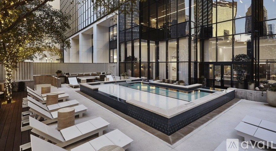 A modern outdoor pool area with sun loungers and a glass wall.
