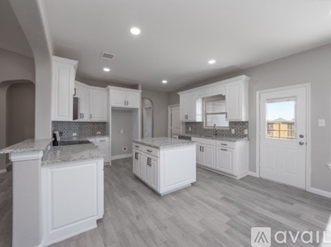 A spacious kitchen with white cabinets and a marble countertop.