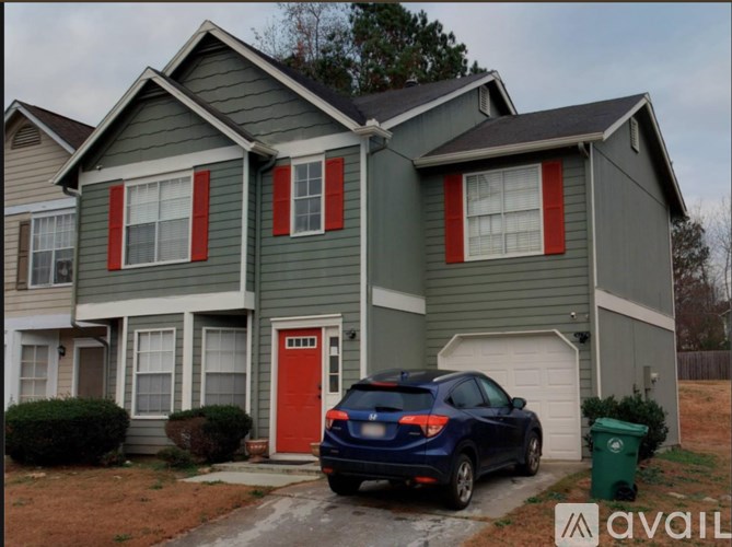 A blue car is parked in front of a grey house with a red door.
