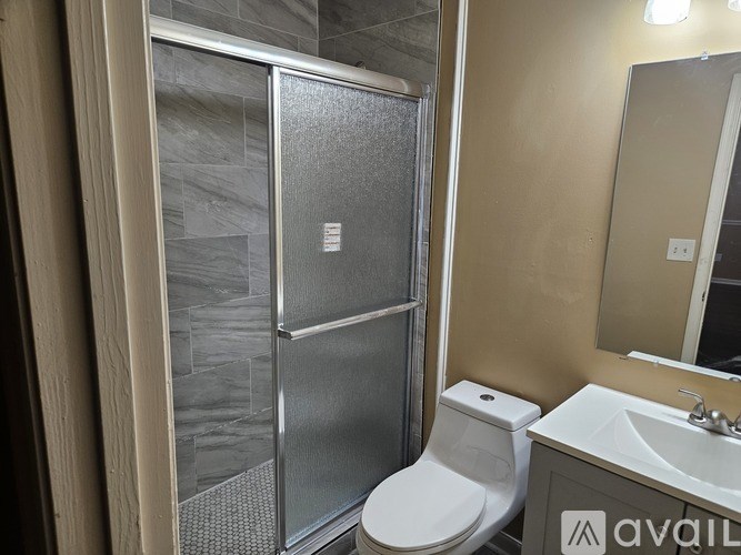 A bathroom with a glass shower stall, toilet, and sink.