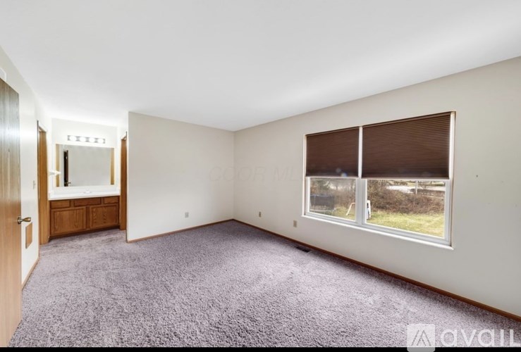 A room with a carpeted floor and a window with blinds.