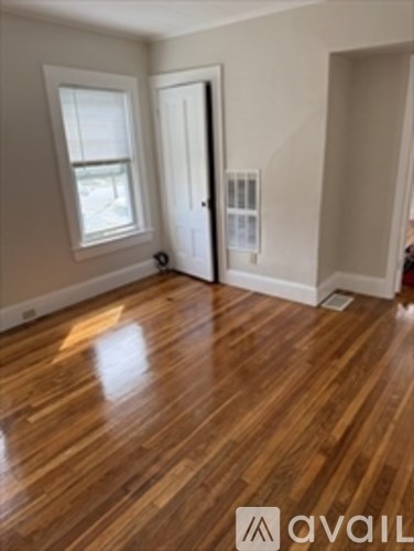 A room with wooden flooring and a door leading to another room.