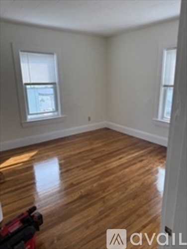 A room with wooden flooring and two windows.