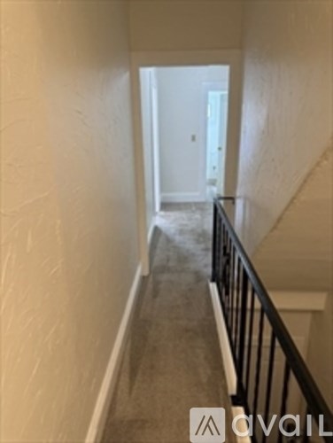 A hallway with a carpeted floor and a black railing.