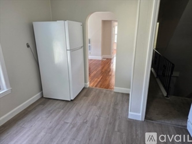 A white fridge in a room with wooden floors and a white wall.