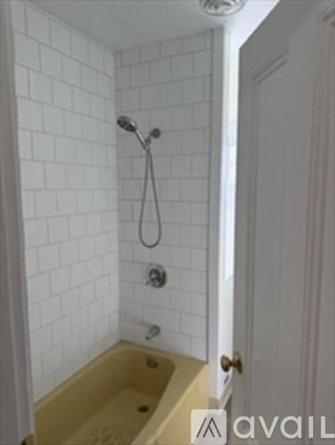 A white tiled bathroom with a yellow tub and a white door.