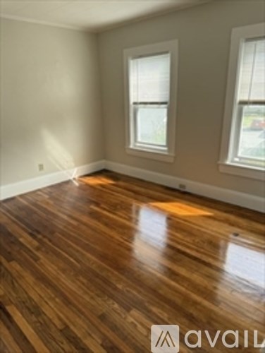 A room with wooden flooring and two windows.