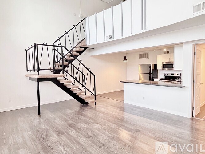 A black metal staircase with a white handrail is in the middle of a white room with a kitchen in the background.
