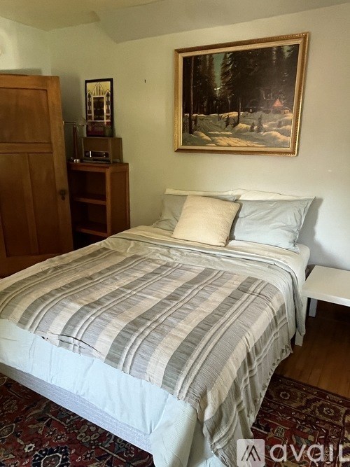 A bed with a striped comforter and two pillows sits in a room with a painting on the wall.
