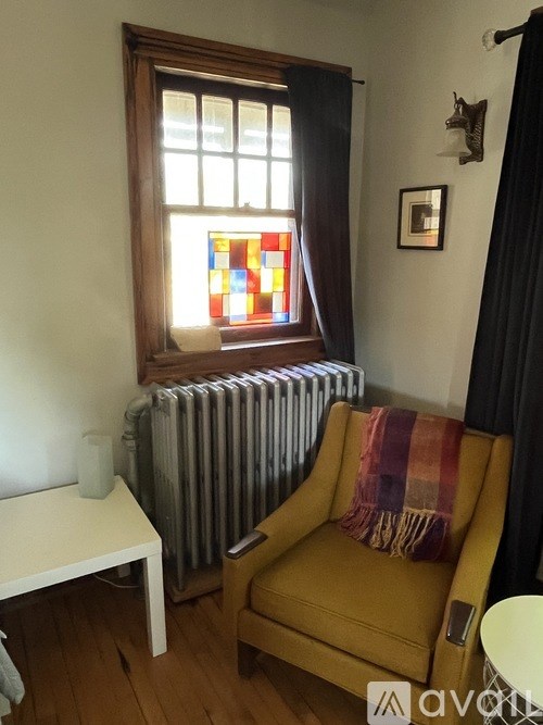A yellow chair with a plaid blanket sits in front of a window with a stained glass design.