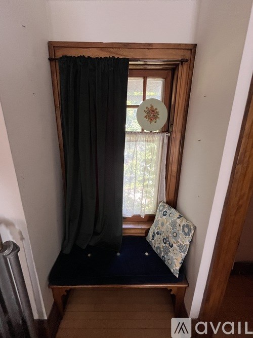 A window with a black curtain and a pillow with a floral pattern.