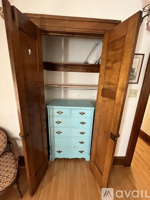 A wooden armoire with a blue dresser inside is open.