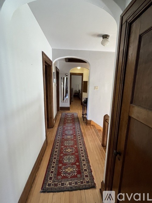 A hallway with a rug on the floor and a wooden door on the right.