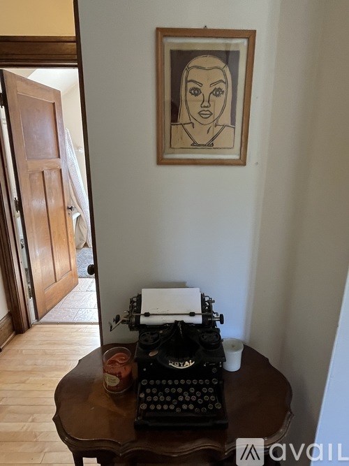 A black typewriter is on a table with a jar of jam and a piece of paper.