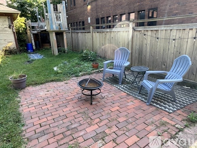 A backyard with a brick patio and two chairs.