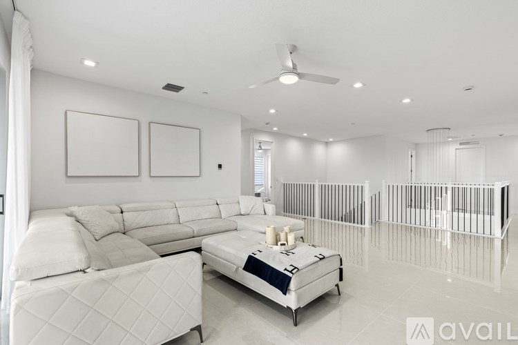 A spacious living room with a white couch, a white bed, and a white ceiling fan.