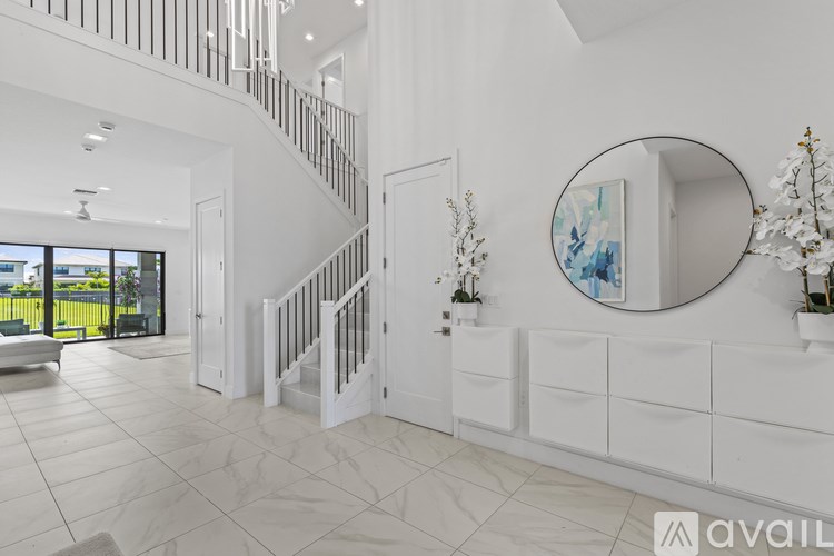 A spacious white hallway with a staircase and a round mirror on the wall.