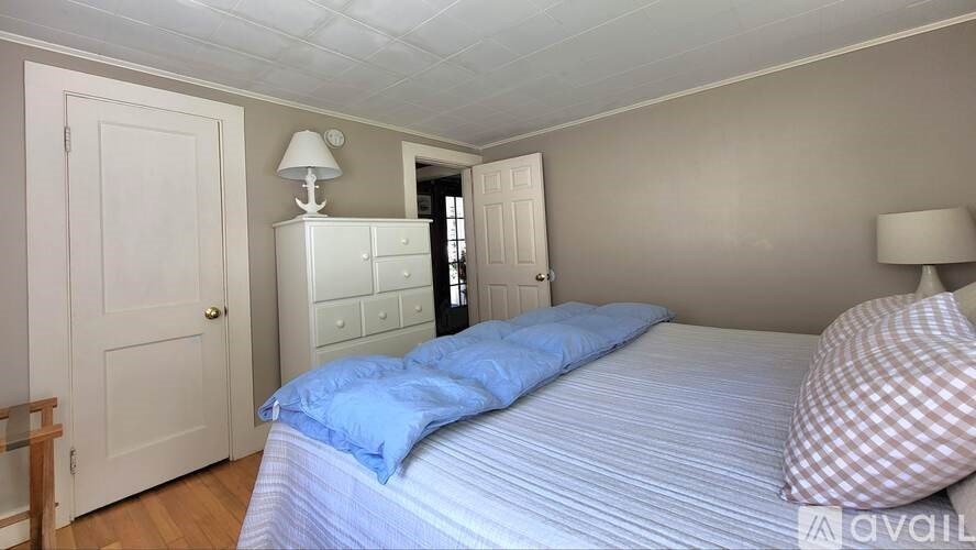 A bedroom with a bed, a nightstand with a lamp, and a door.