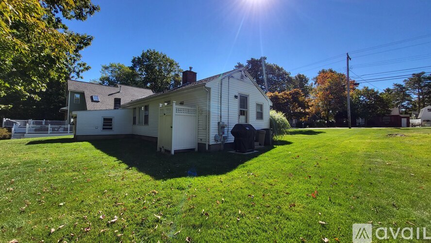 A house with a white exterior is surrounded by a grassy lawn and trees.