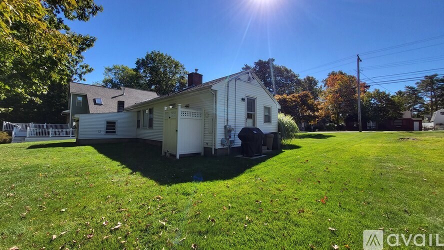 A house with a white exterior is surrounded by a grassy lawn and trees.