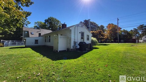 A house with a white exterior is surrounded by a grassy lawn and trees.