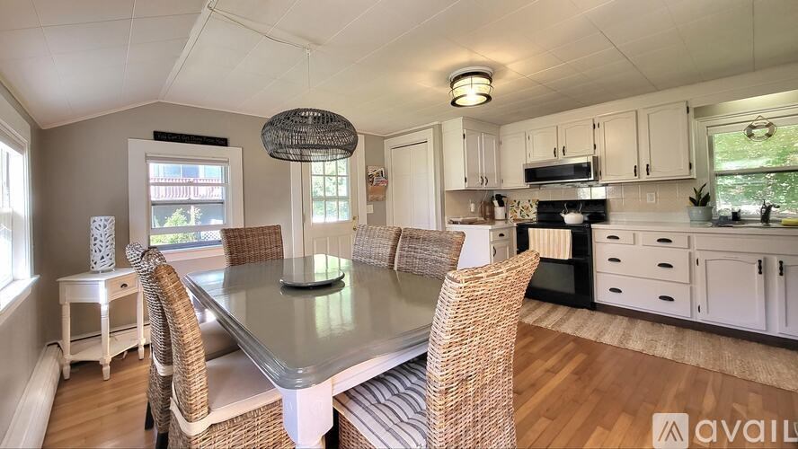 A kitchen with a table and chairs in the foreground and a window with a view of a garden outside.