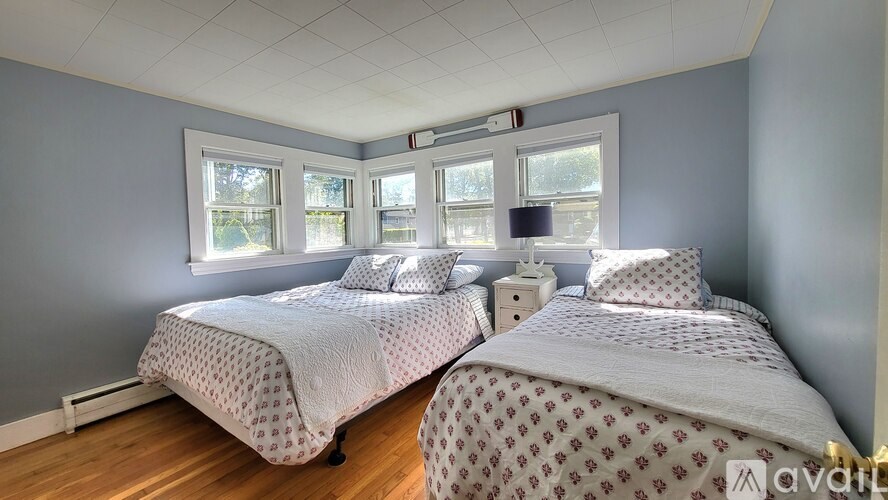 Two beds with white bedspreads and pillows in a room with wooden floors and windows.