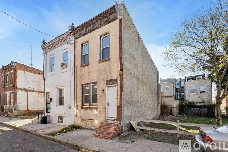 A white two-story building with a brown door and windows is situated on a street corner.