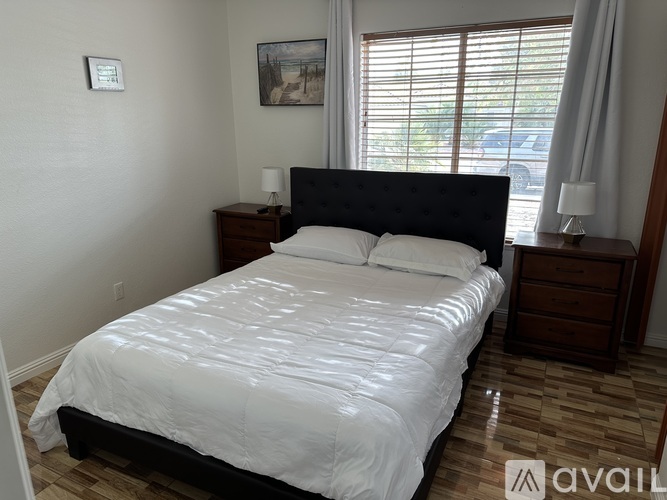A bedroom with a large bed, wooden nightstands, and a window with blinds.