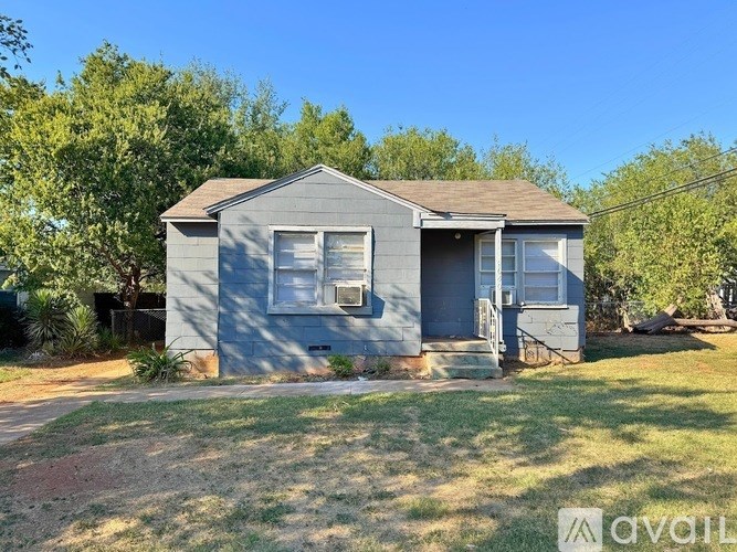 A blue house with a brown roof is surrounded by greenery.