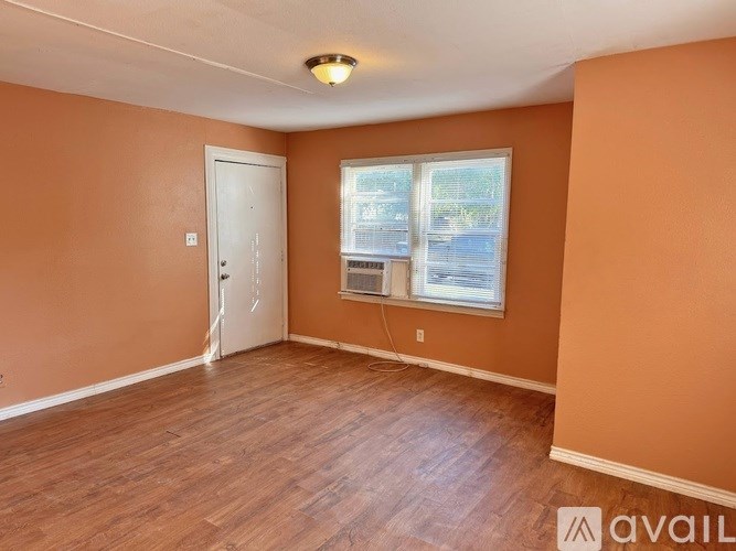 A room with a wooden floor, a white door, and a window with blinds.