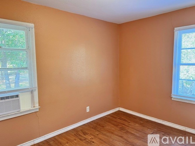 A room with wooden flooring and two windows.