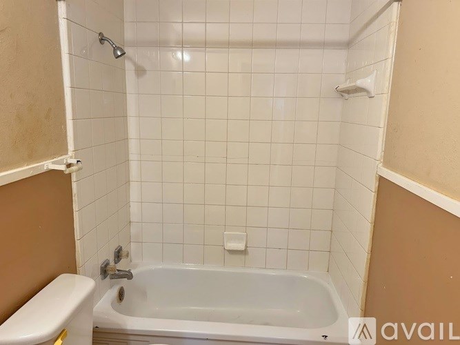 A white bathtub in a bathroom with a shower head and a toilet.