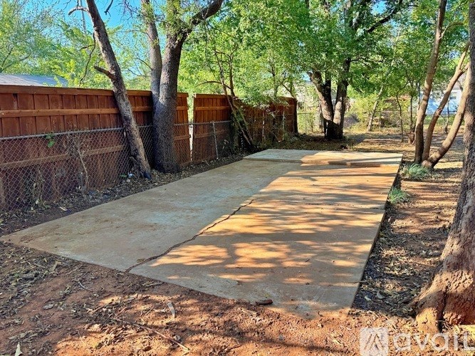 A concrete pathway leads through a backyard with a fence and trees.