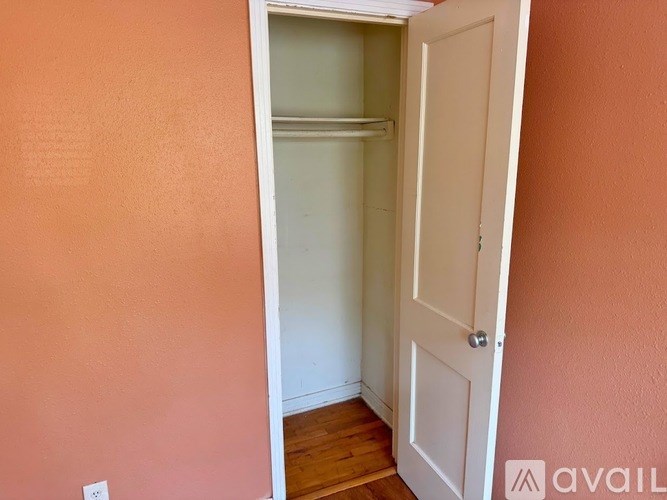 A white door is open to a room with a white wall and wooden floor.