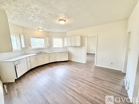 A spacious kitchen with white cabinets and a wooden floor.